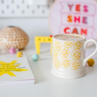 A desk with a book, mug, and a textile weaving that says "Yes she can"