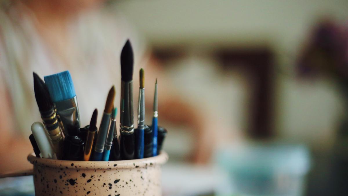 Paint brushes in a pot with artist working in background